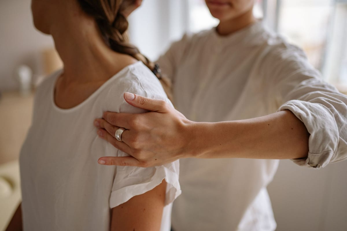 A practitioner's hands placed on a patient's shoulder
