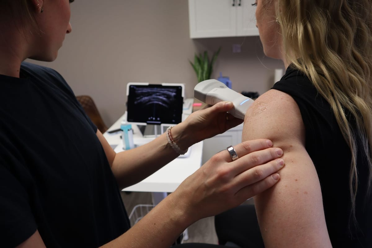 A handheld therapy device being used on a patient's shoulder